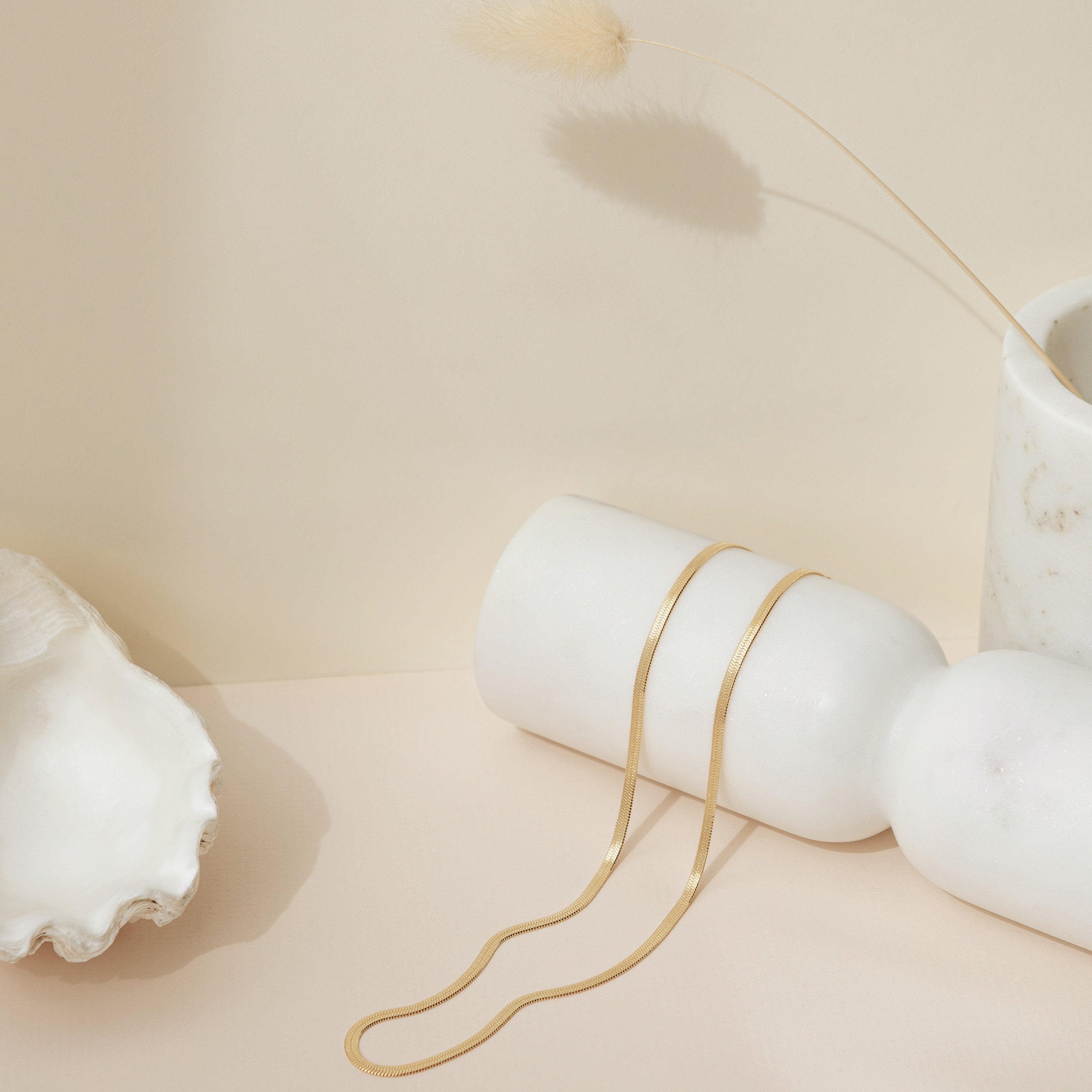 A sleek, gold herringbone necklace displayed draped over a white ceramic vase