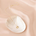 Gold opal medallion necklace with a delicate chain and a sunburst pendant featuring a luminous opal center, styled on a white shell dish atop a soft blush satin background. 