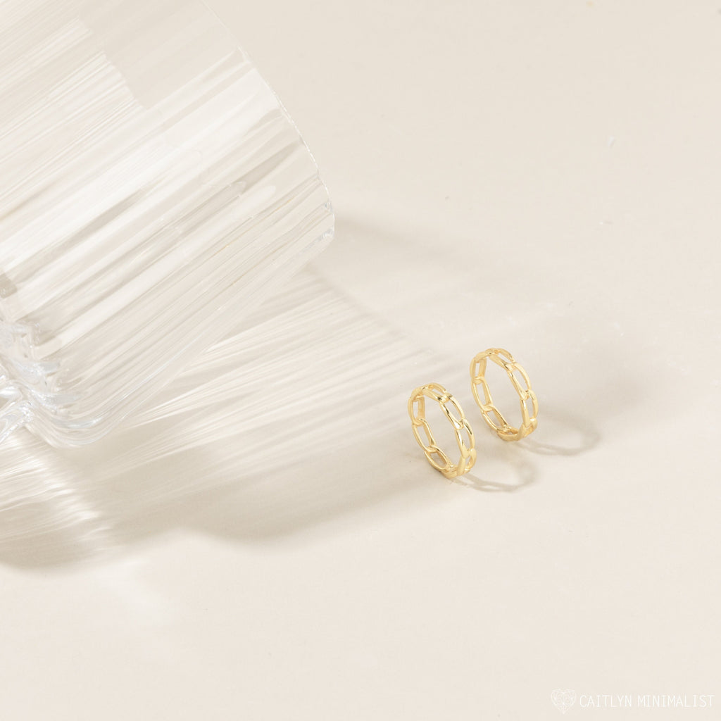 Pair of the gold link rings placed closely together on a fabric backdrop, highlighting the linked design and muted gold tone.