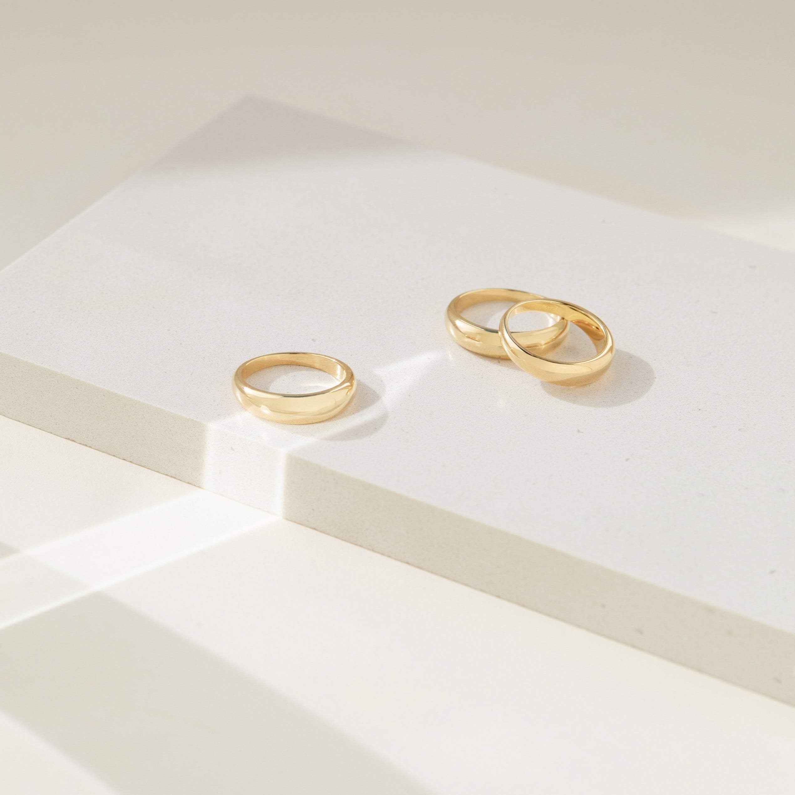 Three of our gold Dome Rings displayed on a minimalist white block with soft natural lighting, showcasing their smooth, polished finish.