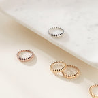 Four Twisted Dome Rings in silver, gold, and rose gold rest on a marble tray and light surface, each showcasing elegant curves and a unique shine.