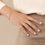 A hand adorned with goth glam jewelry—chunky rings and the Curb Chain Ring—rests on beige pants, complemented by a cream-colored blouse.