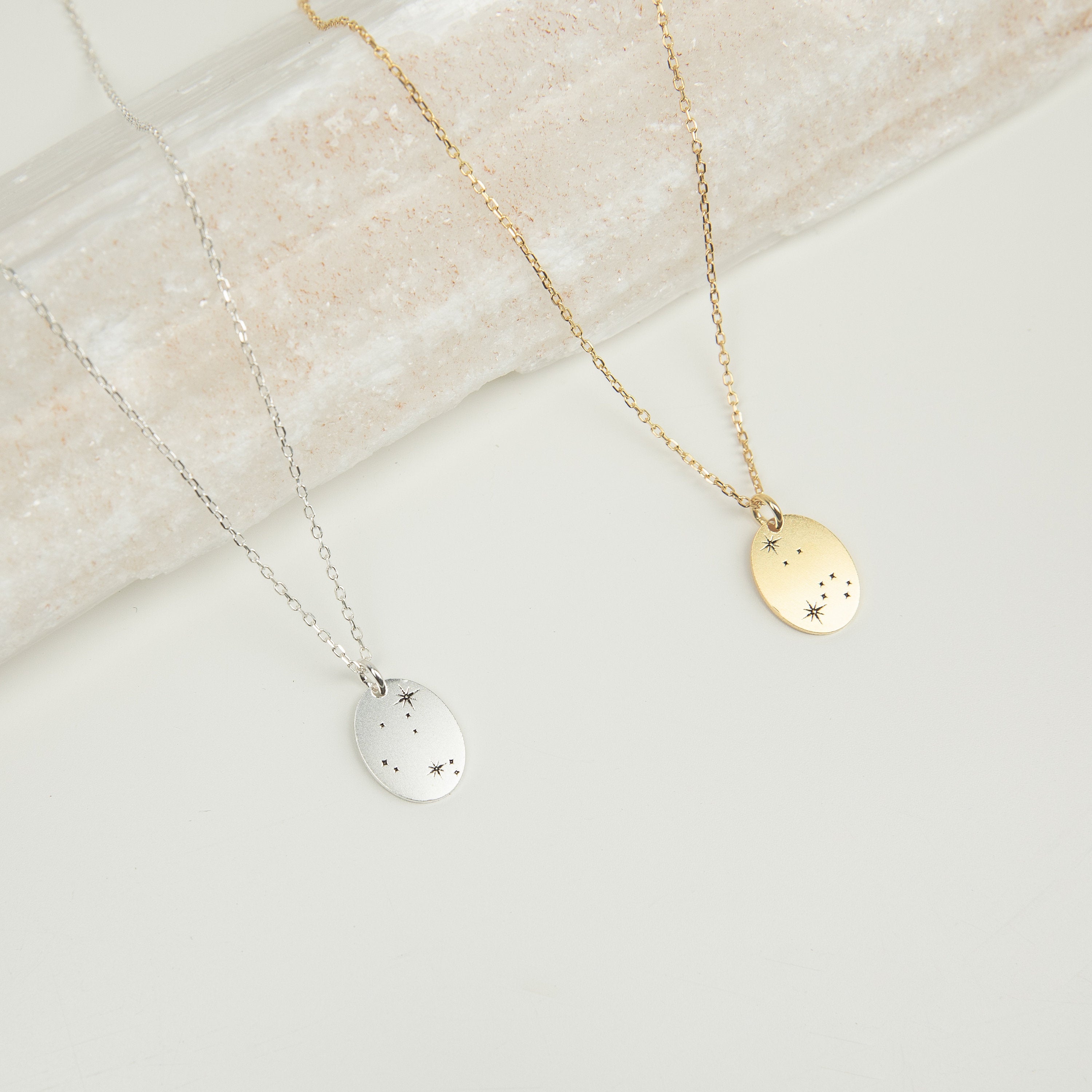 The Zodiac Constellation Necklace features two necklaces—one silver, one gold—with oval pendants engraved with delicate star designs, making it a perfect gift for astrology lovers.