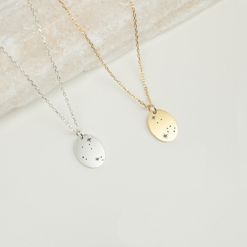 The Zodiac Constellation Necklace features oval pendants in silver and gold, each engraved with delicate star and dot designs, capturing the allure of constellation-inspired amulets.