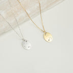 The Zodiac Constellation Necklace features oval pendants in silver and gold, each engraved with delicate star and dot designs, capturing the allure of constellation-inspired amulets.