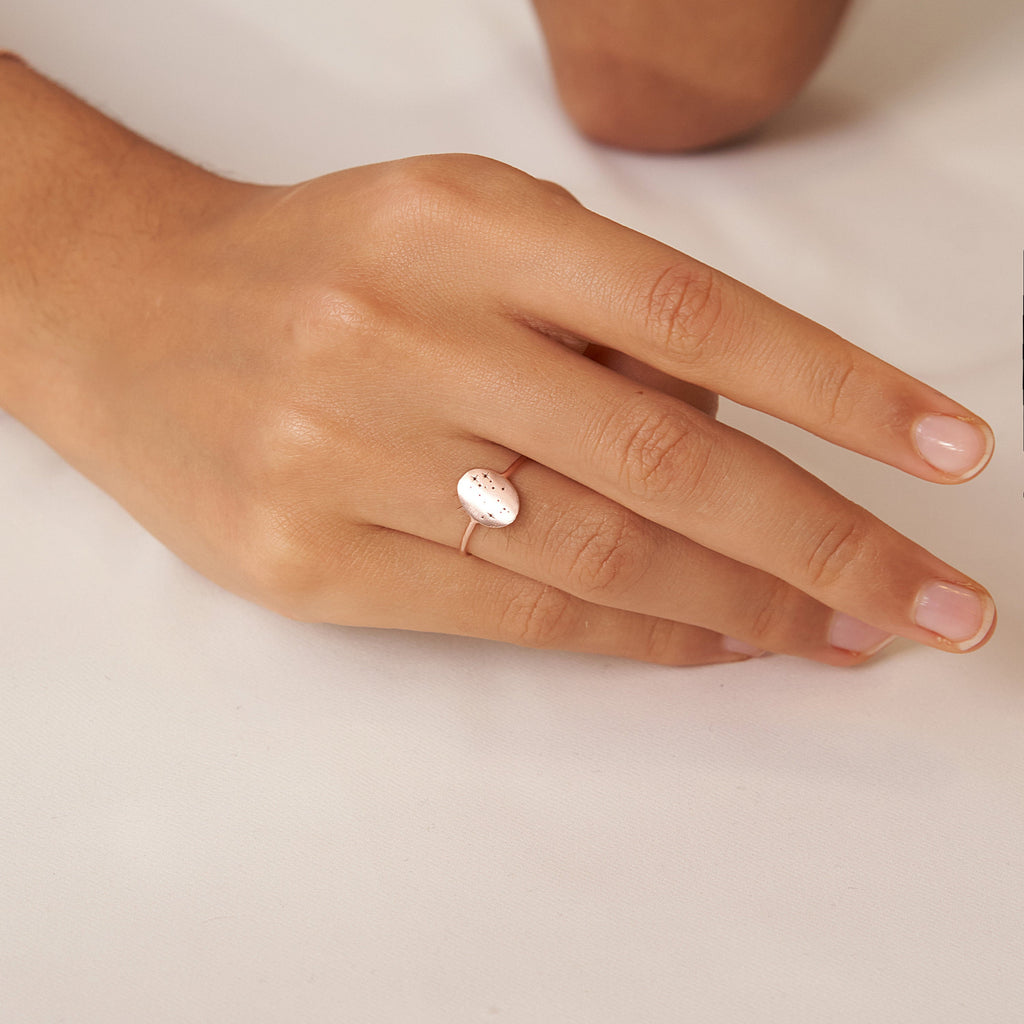 A hand with neatly manicured nails wears the Constellation Oval Ring, a delicate gold zodiac jewelry piece set with an oval white stone.