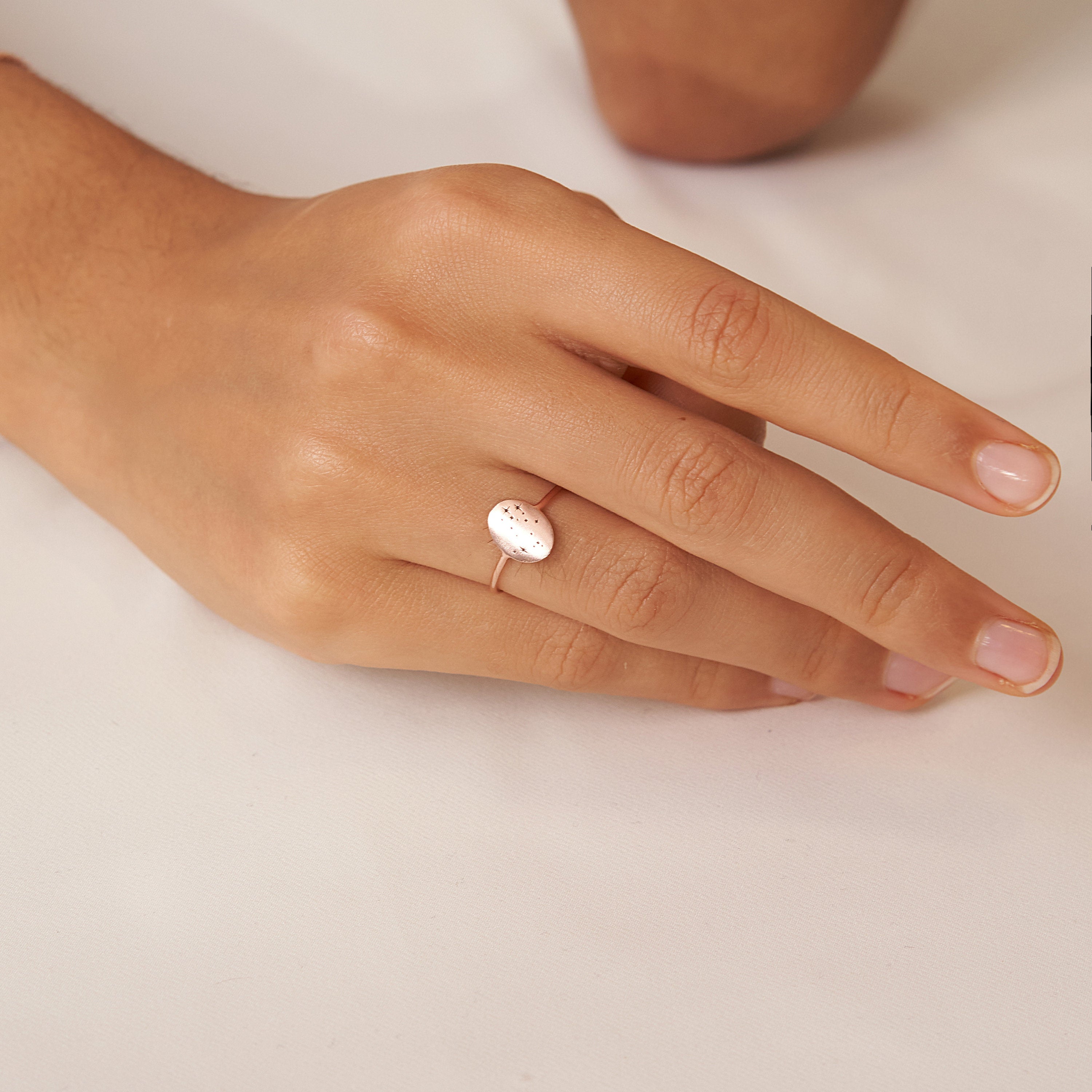 A hand with neatly manicured nails wears the Constellation Oval Ring, a delicate gold zodiac jewelry piece set with an oval white stone.