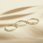 Three Skinny Zodiac Rings, each engraved with an astrological sign, are displayed in a row on a beige surface with soft shadows.