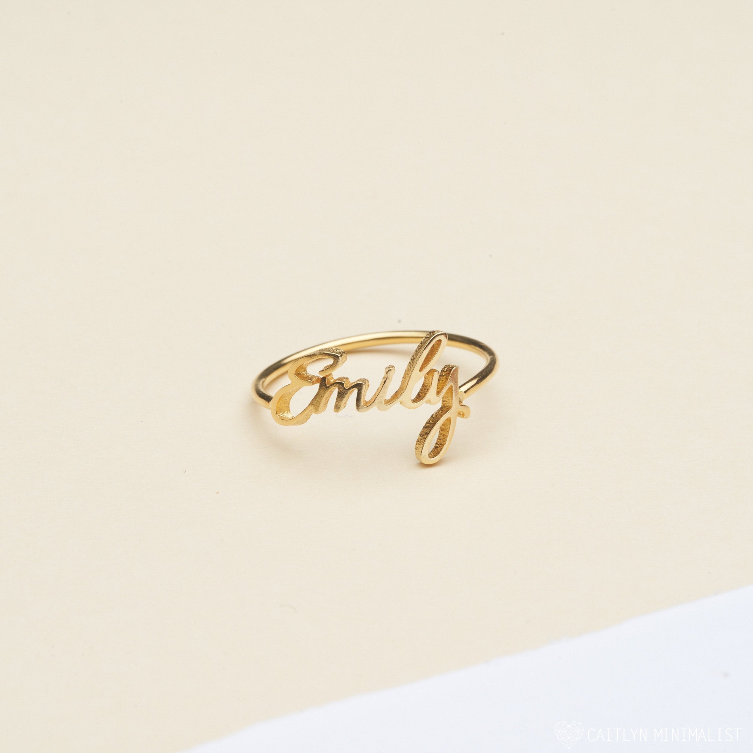 The Grace Script Name Ring features the name Emily in elegant cursive on a cream and white background.