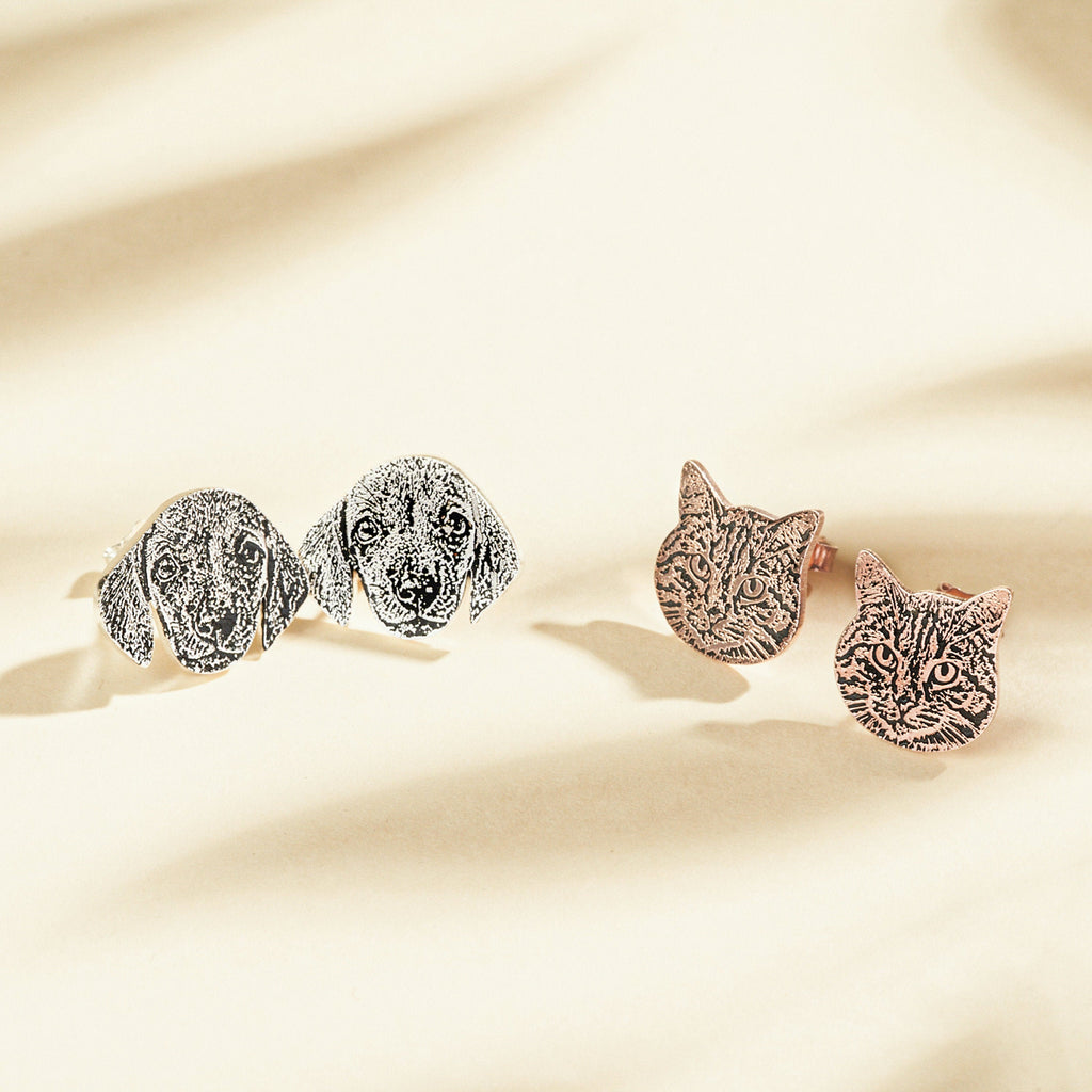 Pet Portrait Studs are engraved metal earrings featuring cat and dog faces—a charming jewelry gift for pet lovers. Displayed on a beige background, these custom earrings celebrate furry friends in style.