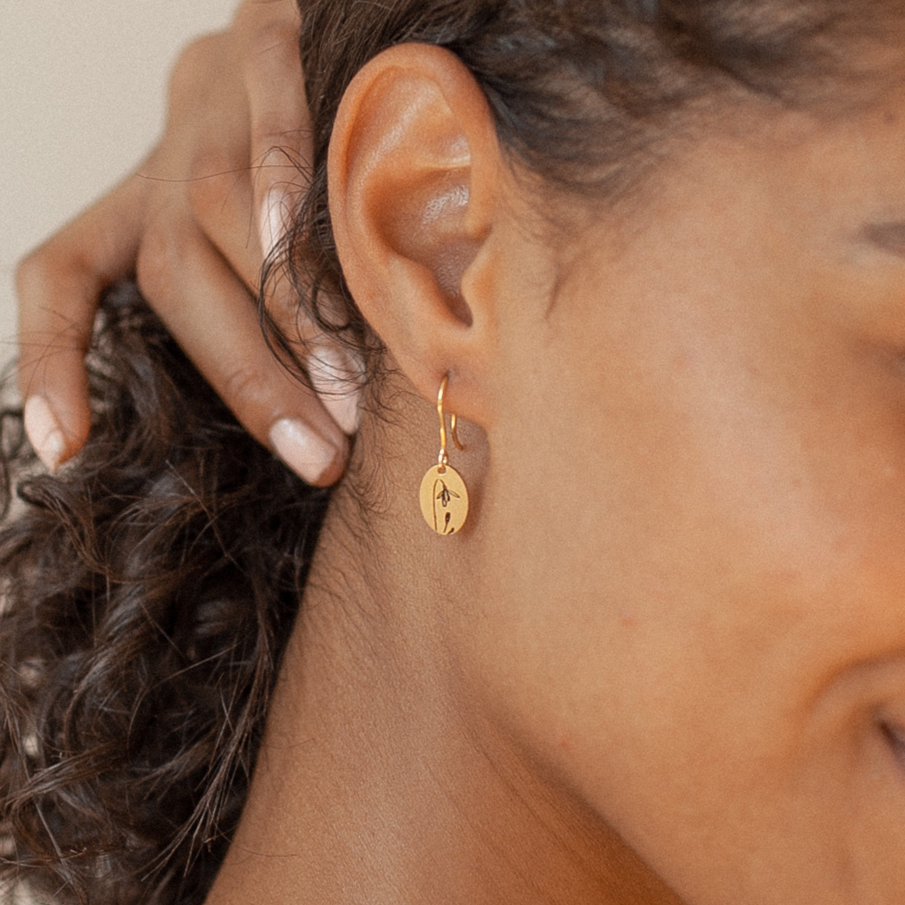 Close-up of a woman wearing Dangling Birth Flower Earrings, gently touching her curly hair.