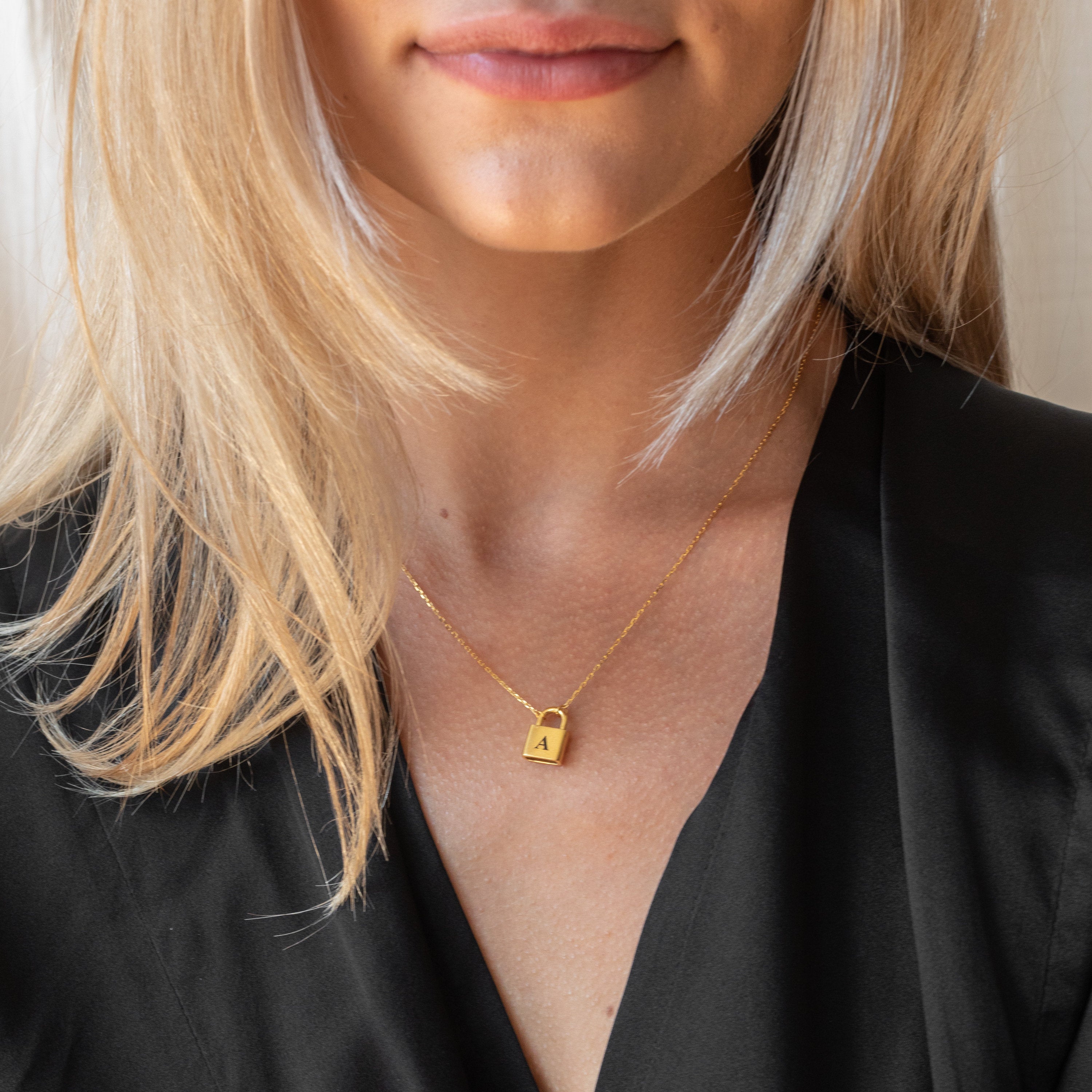 Woman wearing a Padlock Necklace in Rose Gold engraved with the letter “A,” paired with a black top—a chic, initial-themed accessory.
