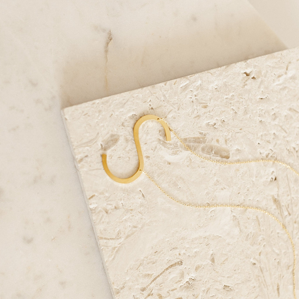 The Large Sideways Initial Necklace features a bold gold letter pendant, beautifully showcased on a textured light stone—making it a standout statement piece.