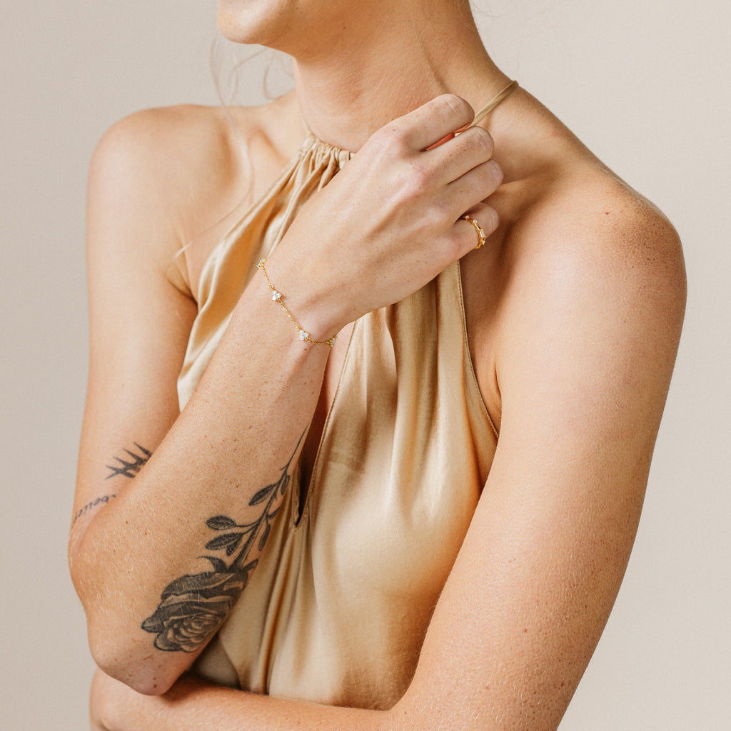 Woman in a gold halter top with a floral arm tattoo, wearing a gold ring and the Mini Lily Diamond Bracelet.