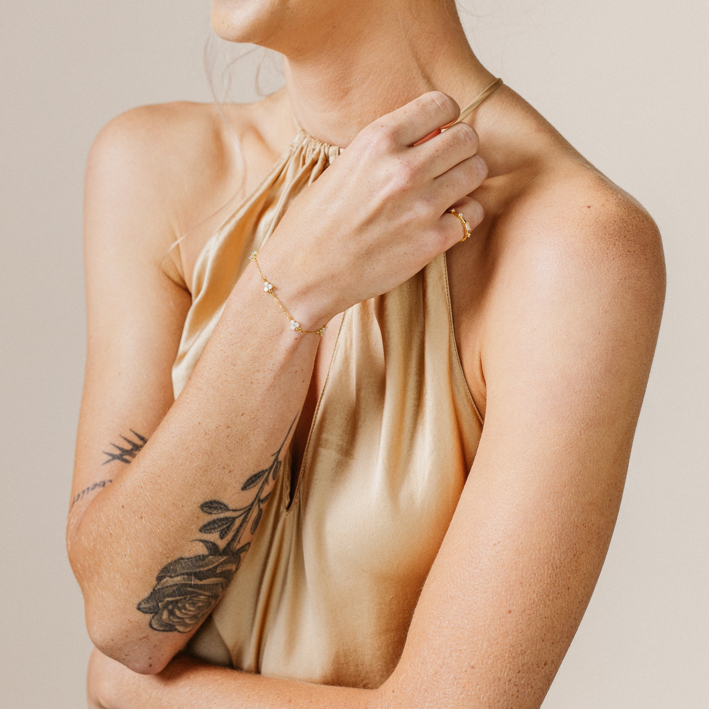 Woman in a gold halter top with a floral arm tattoo, wearing a gold ring and the Mini Lily Diamond Bracelet.