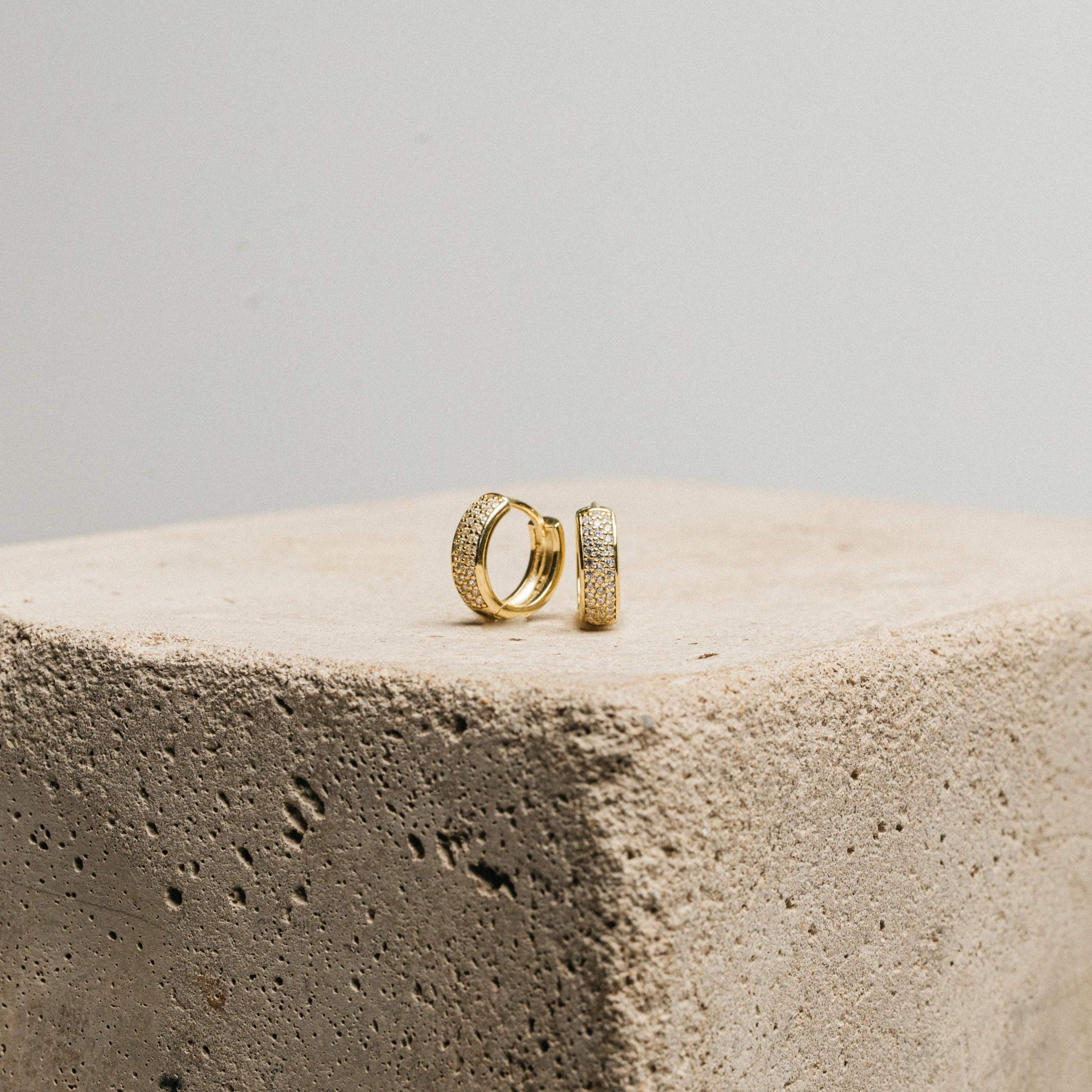 Pave Diamond Huggies rest on a textured stone block against a plain background—an elegant jewelry box essential, featuring sparkling diamond-encrusted hoops.