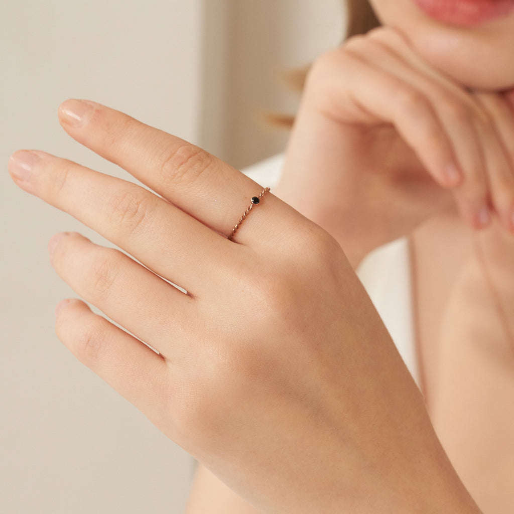 The Twisted Birthstone Ring, featuring delicate gold beads, elegantly adorns a woman's finger—ideal for stacking with your favorite rings.