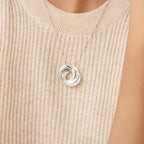 The Interlocking Family Necklace shimmers over a beige ribbed knit top, its silver rings personalized with words that celebrate family bonds.