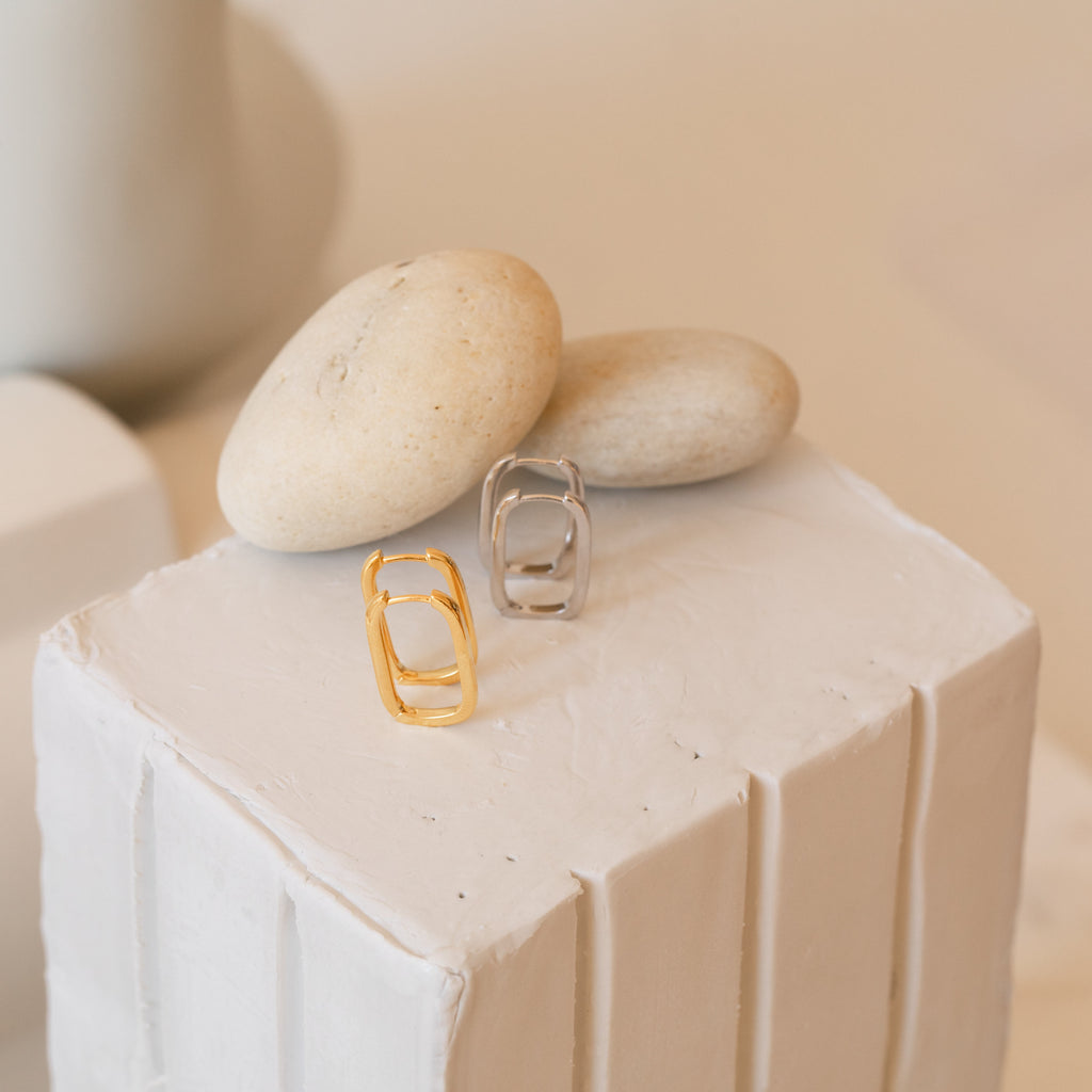 Nina Link Earrings in Sterling Silver displayed on a white textured block with smooth beige stones.