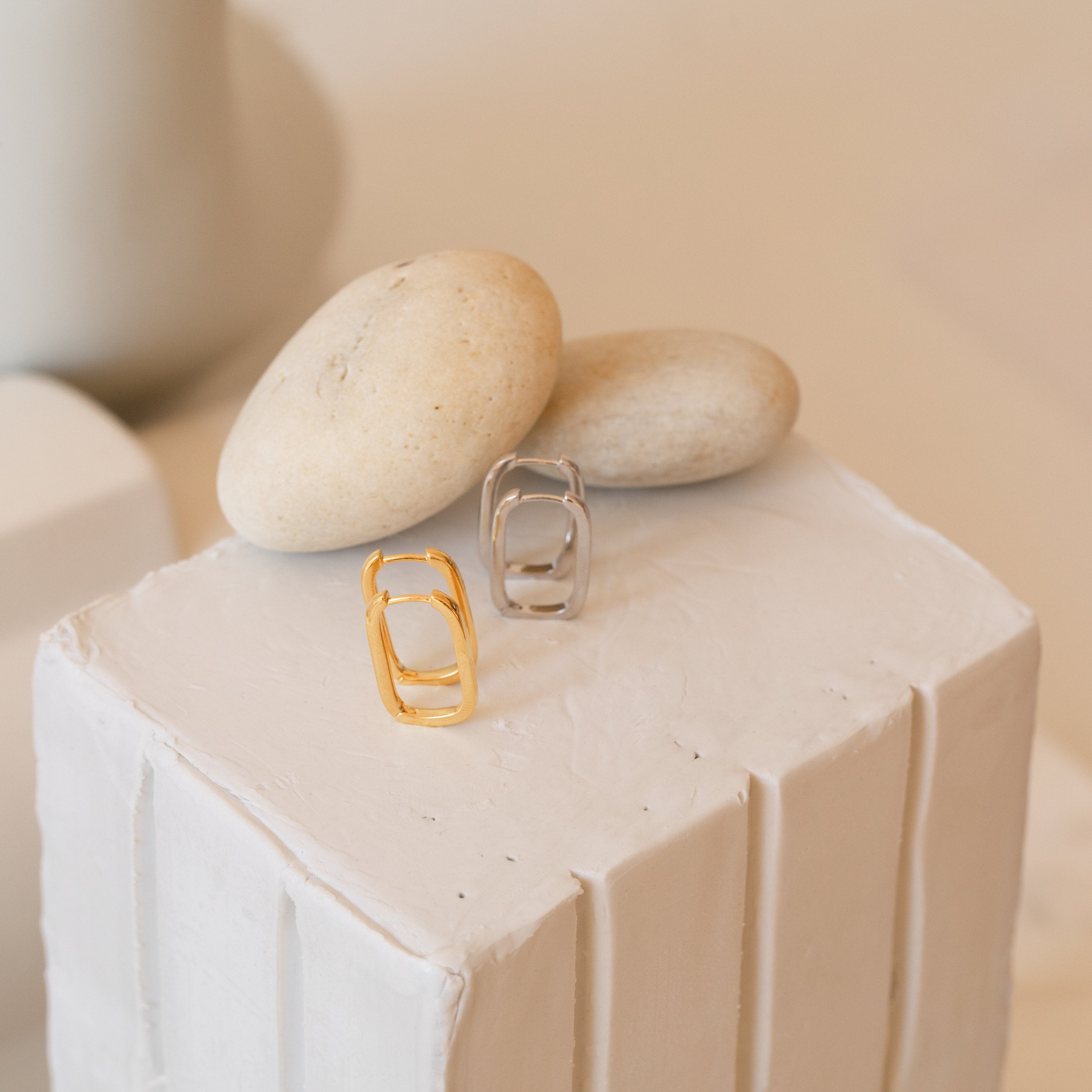 Nina Link Earrings in Sterling Silver displayed on a white textured block with smooth beige stones.