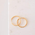 Two sterling silver Classic Hoops earrings rest elegantly on a white marble surface—perfect for the modern city girl.