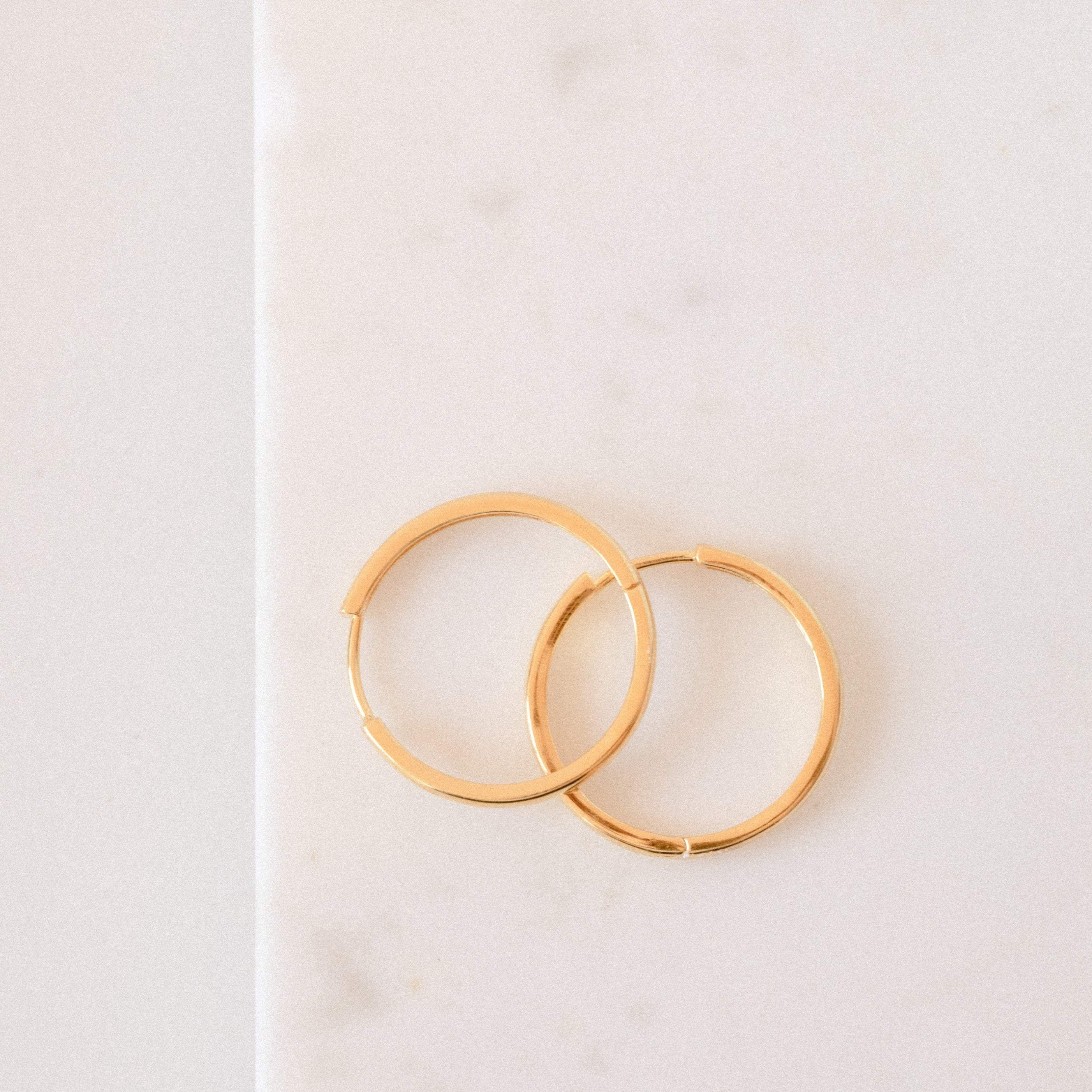 Two sterling silver Classic Hoops earrings rest elegantly on a white marble surface—perfect for the modern city girl.