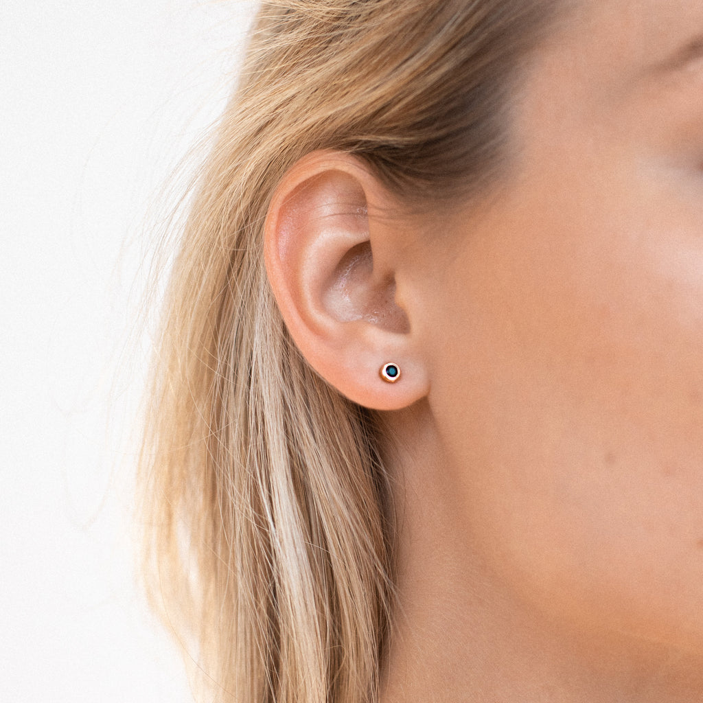 Close-up of a woman's ear wearing Noir Diamond Studs—small, round black diamond earrings that add a unique touch to her style.