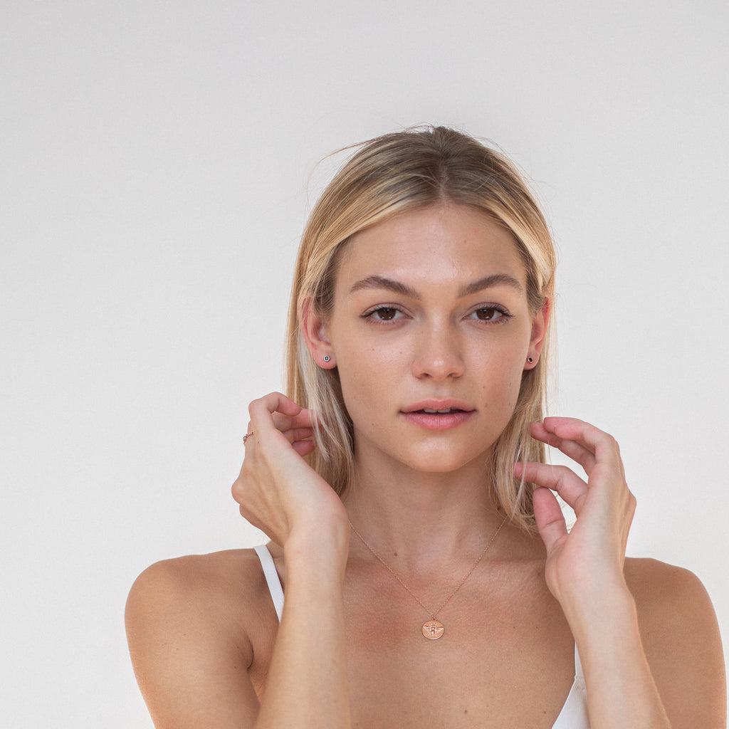 A woman with blonde hair poses against a plain background, wearing a necklace, a white top, and Noir Diamond Studs earrings that add a touch of elegance to her look.