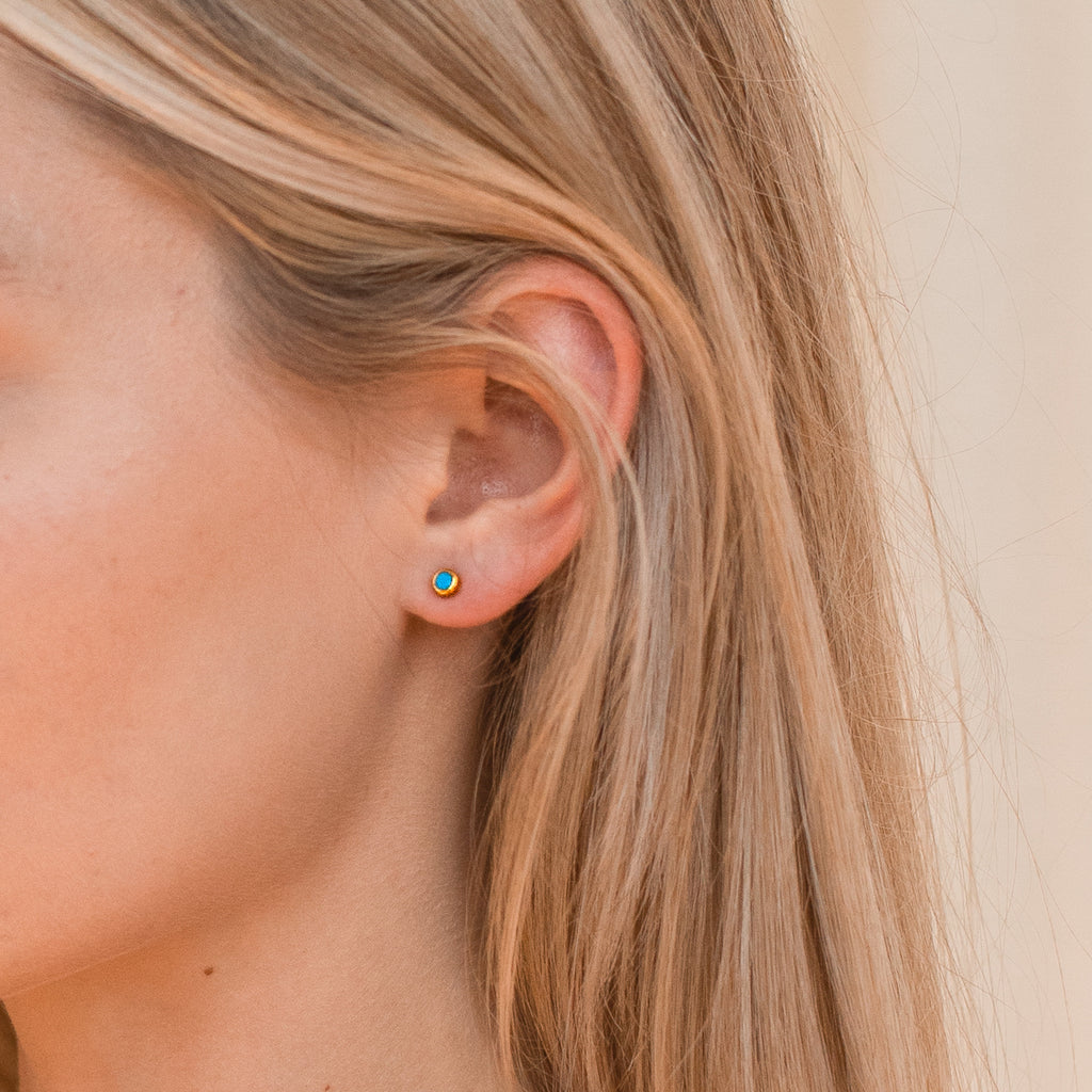 Close-up of a woman’s ear wearing Ariel Turquoise Studs; her straight blonde hair is tucked behind her ear, drawing attention to the dainty, round turquoise earrings.
