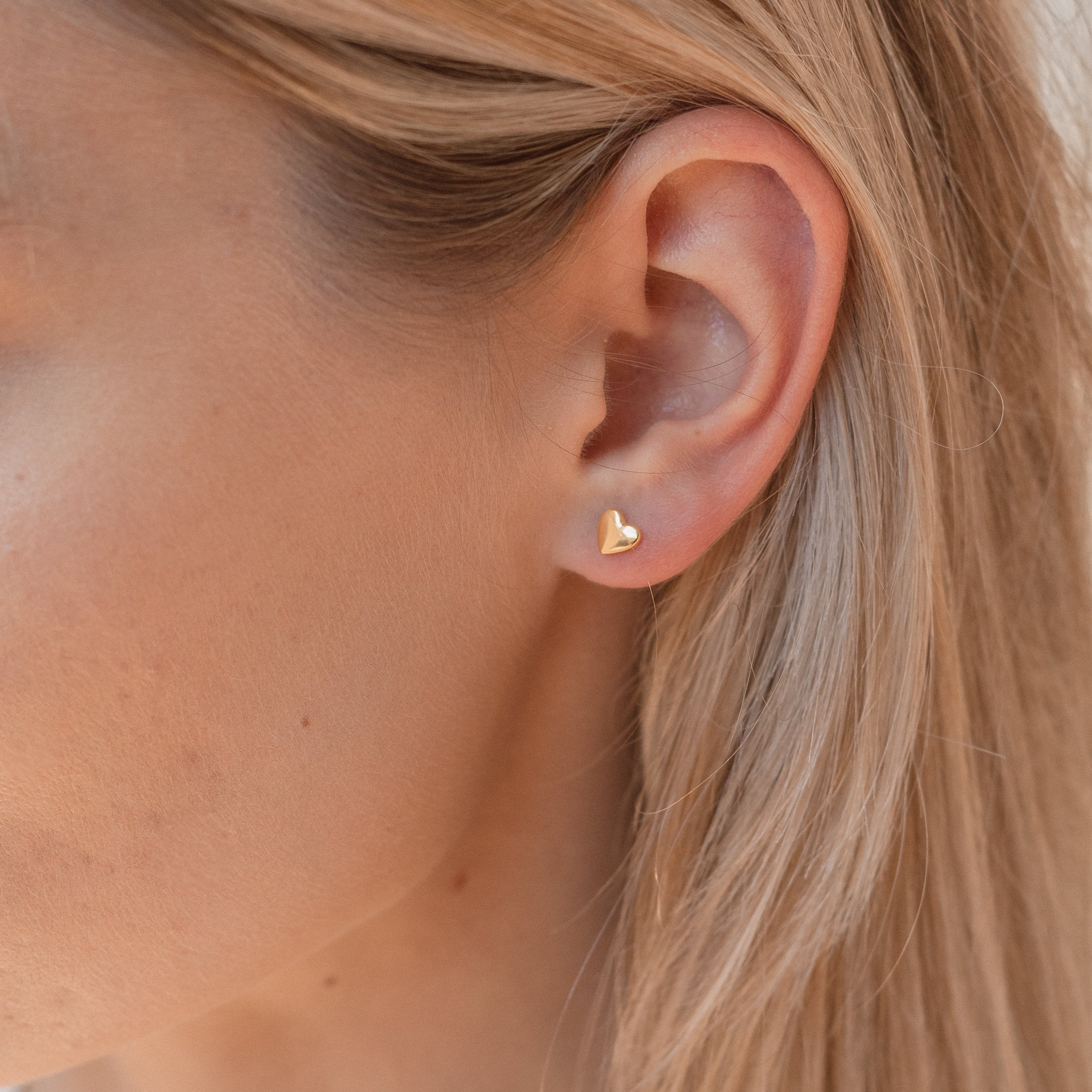 Close-up of a woman's ear wearing the Classic Heart Studs—small gold earrings that are dainty, cute, and perfect for anyone who loves charming accessories.