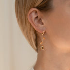 Close-up of a woman wearing Dangling Rose Huggies with her hair tucked behind her ear—a romantic and elegant gold rose-shaped earring.