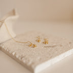 Dangling Rose Huggies displayed on a textured white stone with a soft background, offering a touch of romantic jewelry elegance.