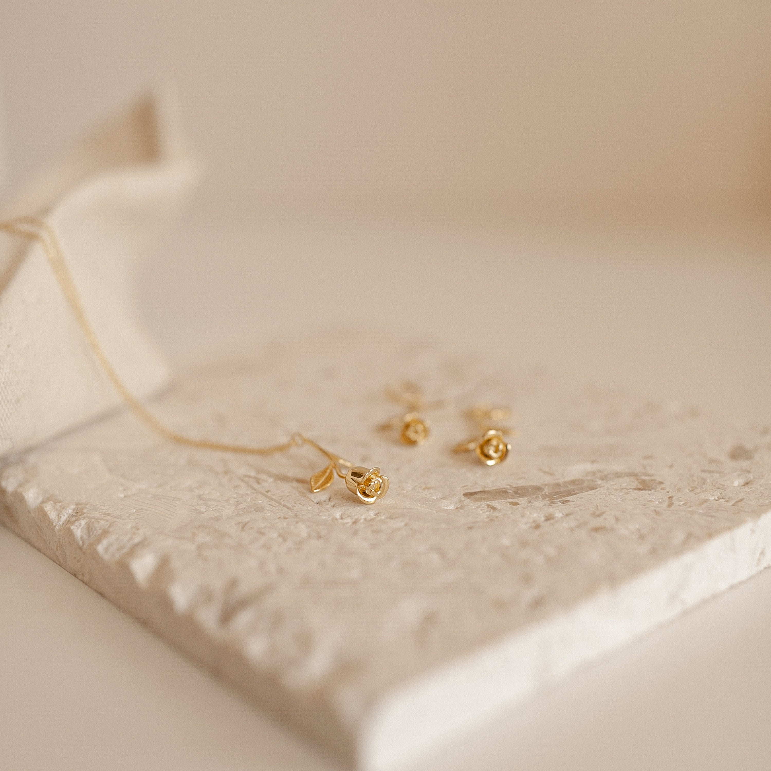 Dangling Rose Huggies displayed on a textured white stone with a soft background, offering a touch of romantic jewelry elegance.