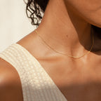The gold Satellite Necklace worn close to the neck by a model in a cream textured top, under warm natural light.