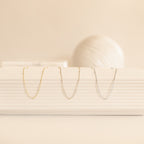 Three Satellite Necklaces—yellow gold, rose gold, and white gold—are displayed hanging neatly from a white ribbed ceramic display.