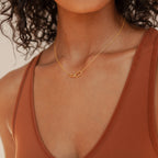 A woman wears the Linked Pendant Necklace, a delicate geometric gold chain, paired with a rust-colored tank top.