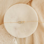 Linked Pendant Necklace featuring a delicate rectangular pendant on a thin gold chain, elegantly displayed on a round white stone background—a subtle symbol of love.