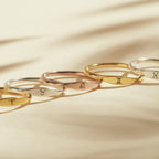 Five Skinny Zodiac Rings with engraved zodiac symbols are arranged in a row on a beige surface, illuminated by soft lighting.
