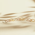 Nine Skinny Zodiac Rings in gold and silver are neatly arranged on a beige surface, with soft shadows in the background.