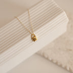 Padlock Necklace: Gold necklace featuring a padlock pendant engraved with the letter E, perfect for adding a chic touch to any look. Shown on a textured white background.