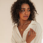 Woman with curly hair in a white shirt wears the Name Tag Necklace in Rose Gold, looking to the side against a neutral background.