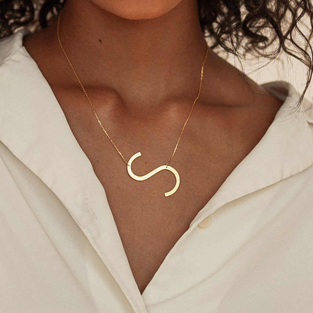 A woman wears a white shirt and the Large Sideways Initial Necklace in Rose Gold, featuring a bold letter pendant that makes it a true statement piece.