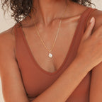 Gold paperclip chain necklace featuring a single baroque freshwater pearl pendant, worn centered on the chest. Styled with a rust colored V neck tank top.