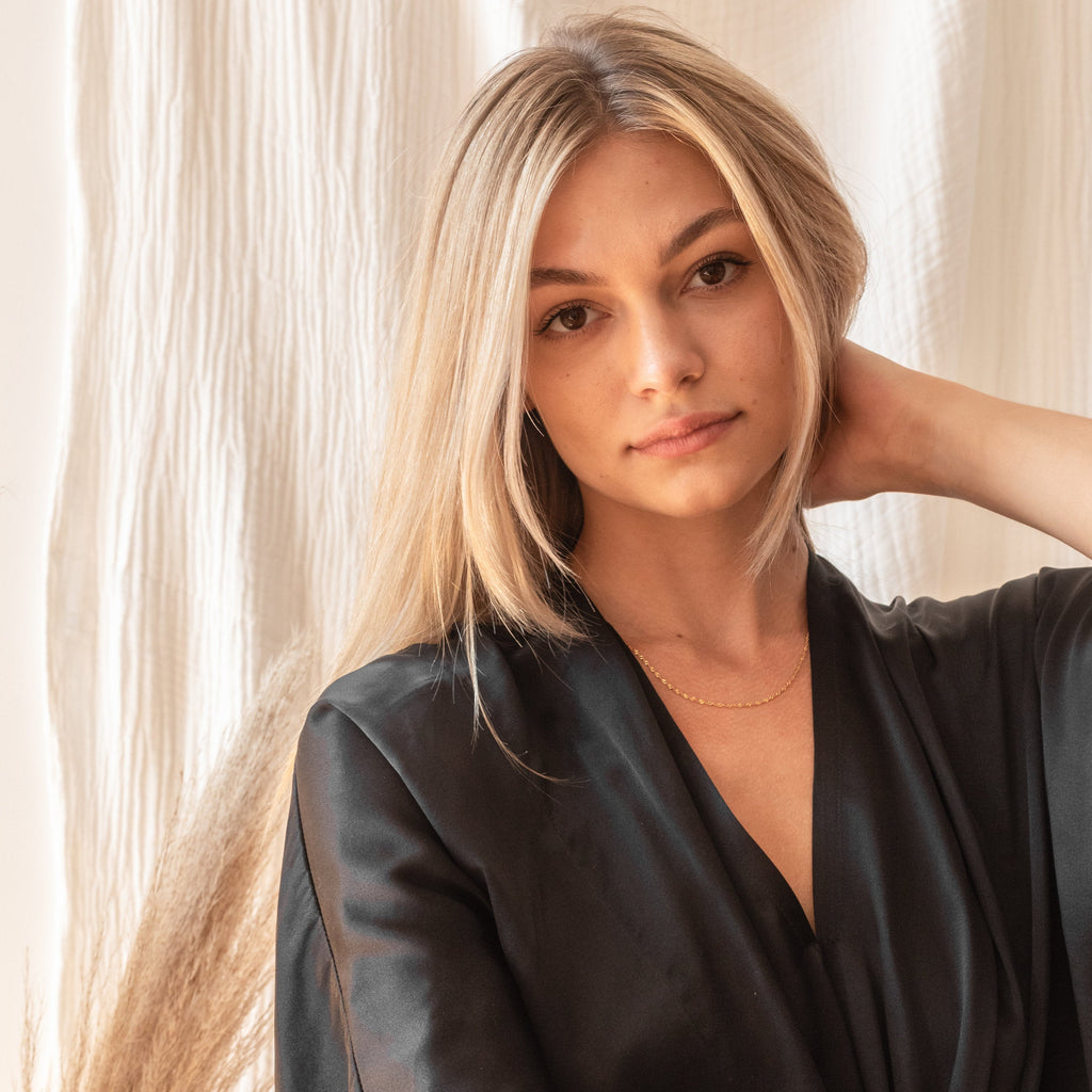 A portrait of a model in a black robe, wearing the Singapore Twist Necklace for a minimal, elegant finish.