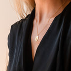 A woman in a black top wears the Bee Coin Necklace, featuring a gold round pendant—perfect for layering.