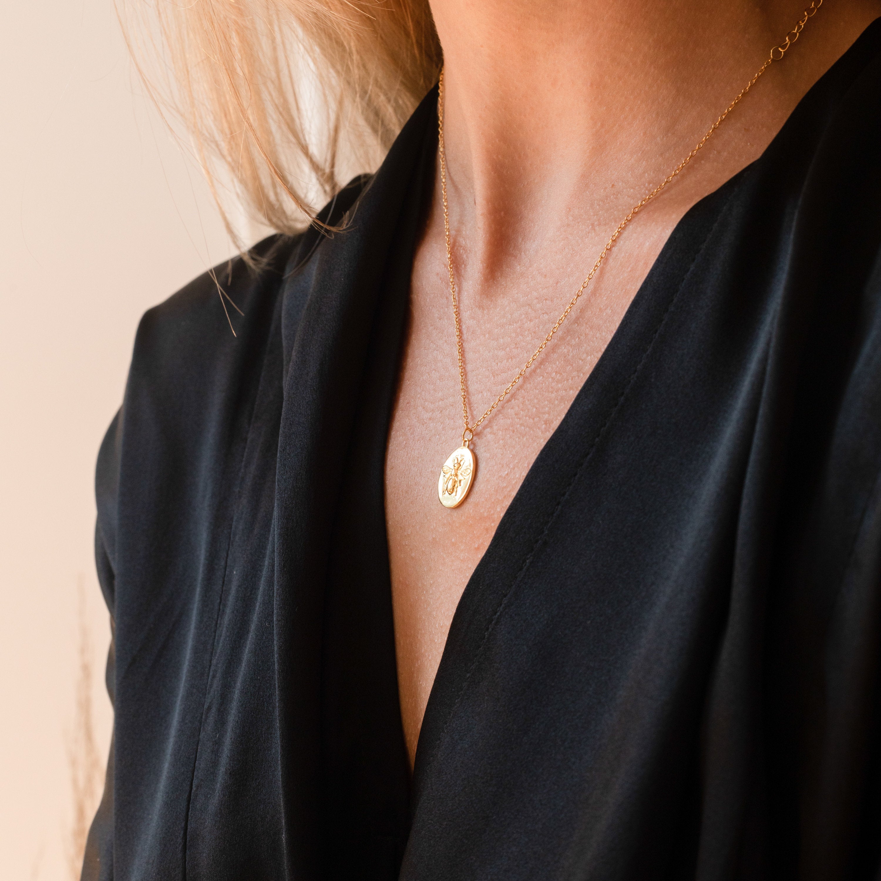 A woman in a black top wears the Bee Coin Necklace, featuring a gold round pendant—perfect for layering.