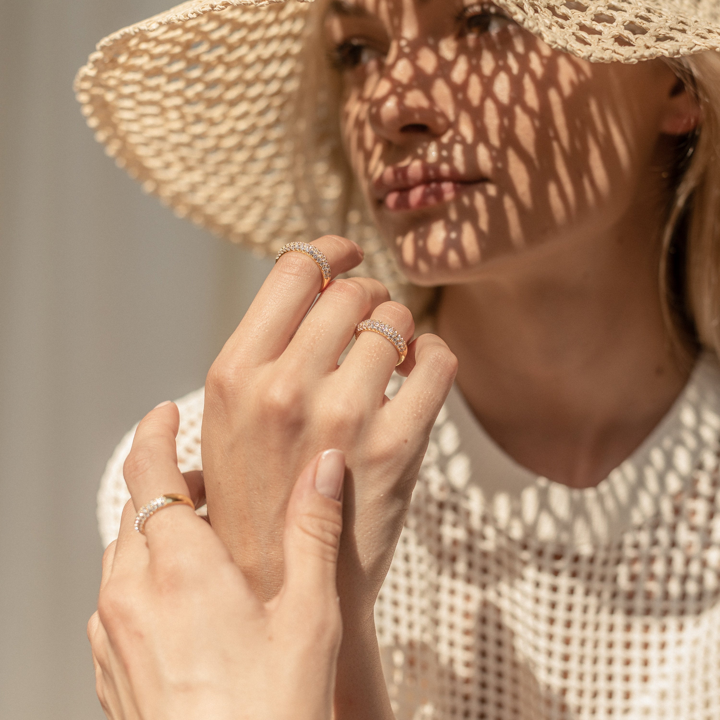 A woman wearing a sunhat and the Pave Dome Ring, sunlight casting patterned shadows across her face and hands.