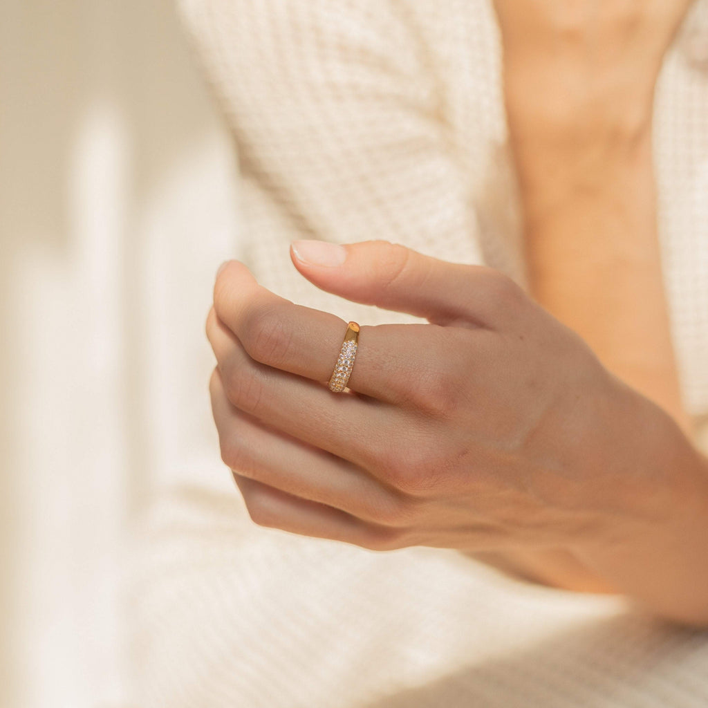 A hand wears the Pave Dome Ring, featuring gold and sparkling diamonds, against a softly blurred background.
