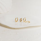 The Cleo Cuffs set features four small gold hoops, including stylish ear cuffs and cartilage earrings, displayed on a white ceramic dish against a neutral background.