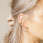 Close-up of a woman’s ear wearing Cleo Cuffs gold hoop earrings—one on her cartilage and one on her earlobe.